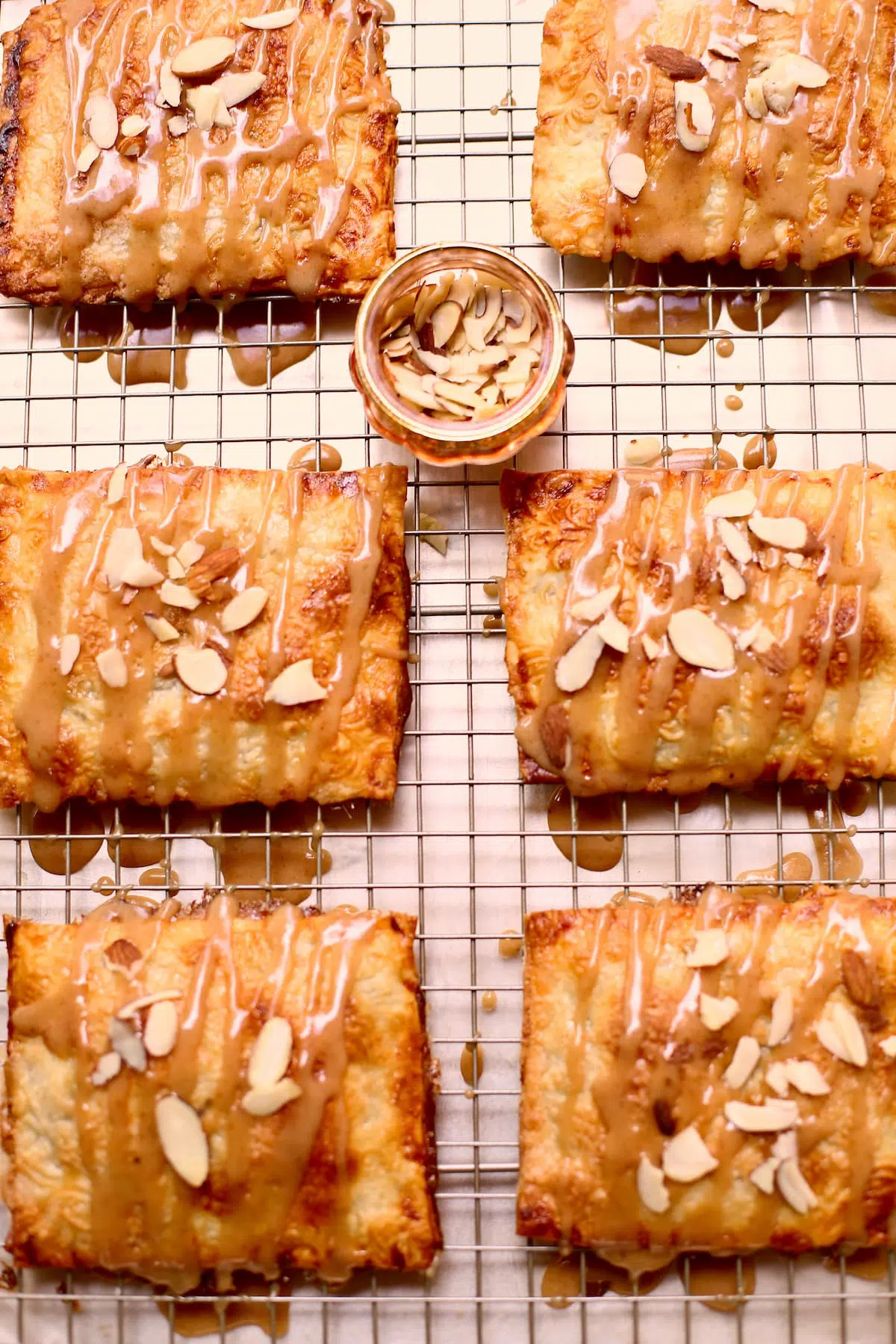 a wire rack of hand pies with a small cup of sliced almonds in the middle. s
