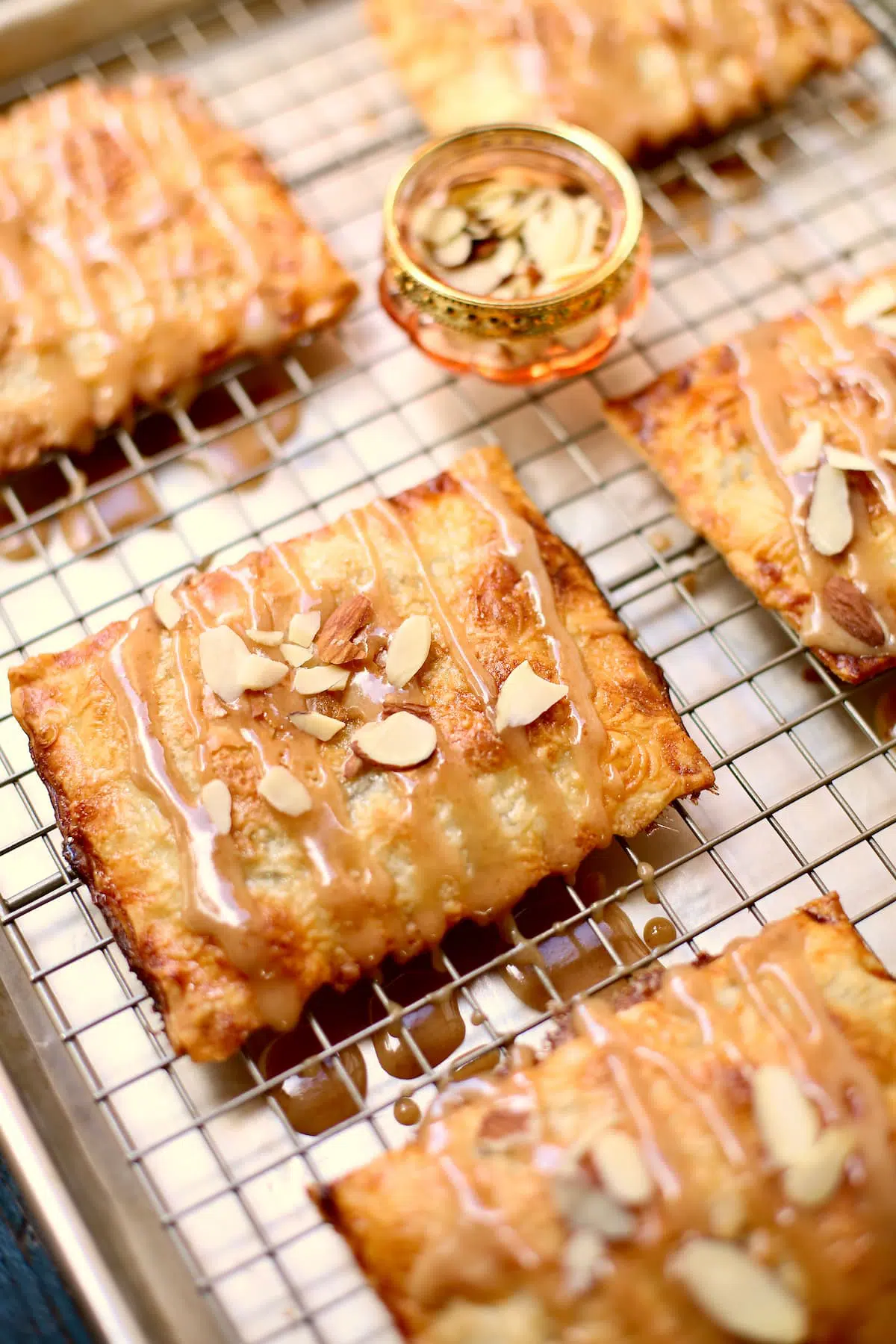 a wire cooling rack of hand pies with a drizzle of icing and sprinkle of almonds.