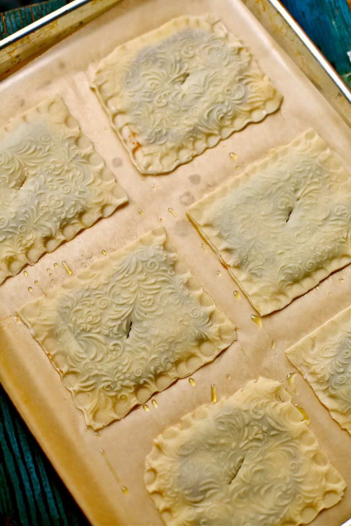a baking sheet with parchment paper of square, unbaked hand pies with a crimped edge and pattern to the pastry.