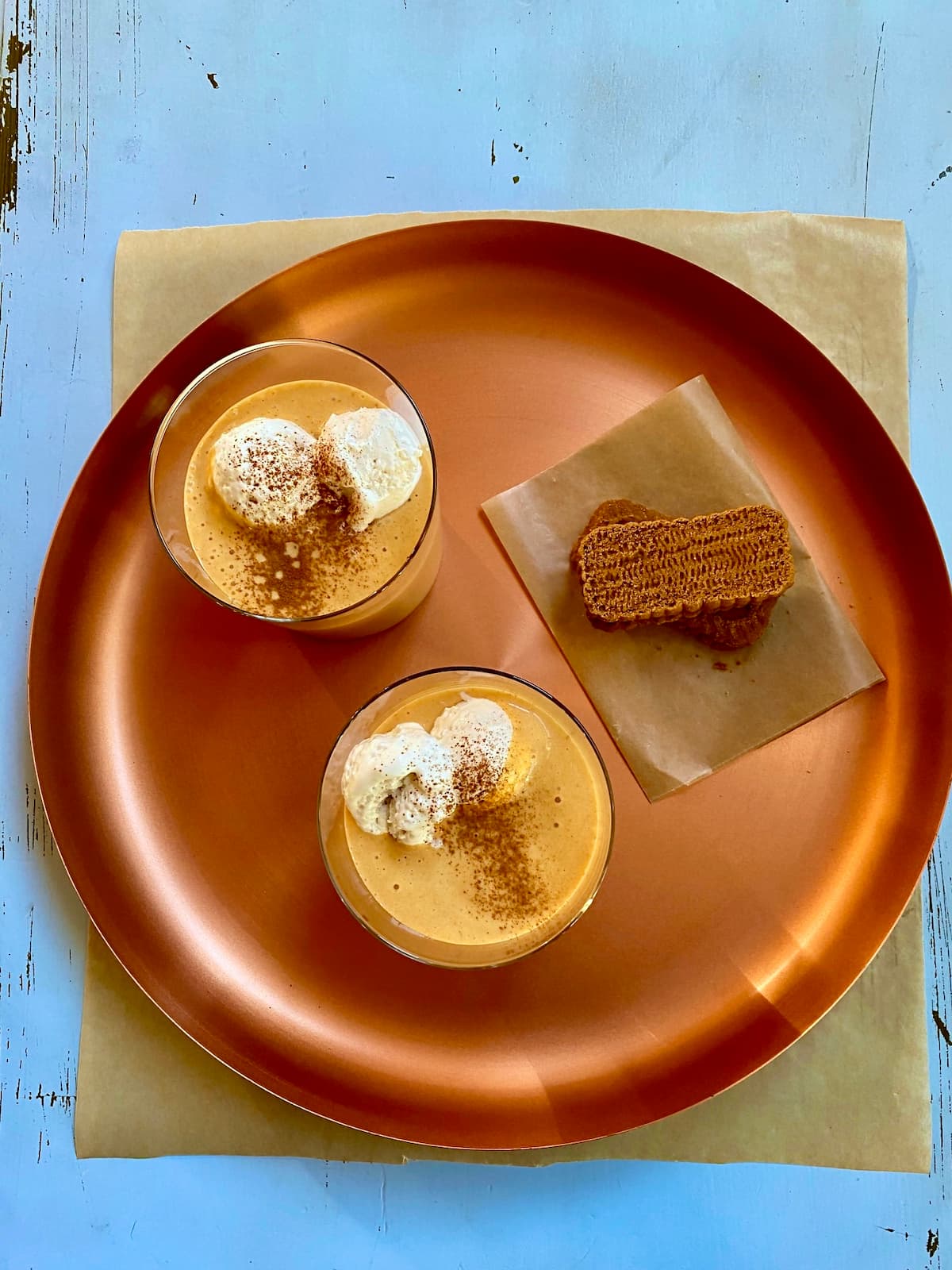 a copper tray with two orange milkshakes and two graham crackers on a blue table.