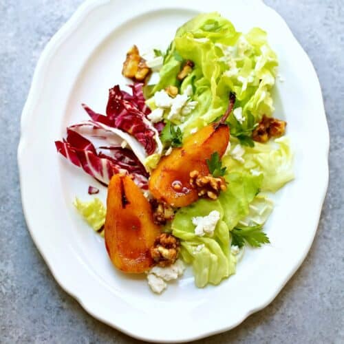 a pear and green salad on a white plate.