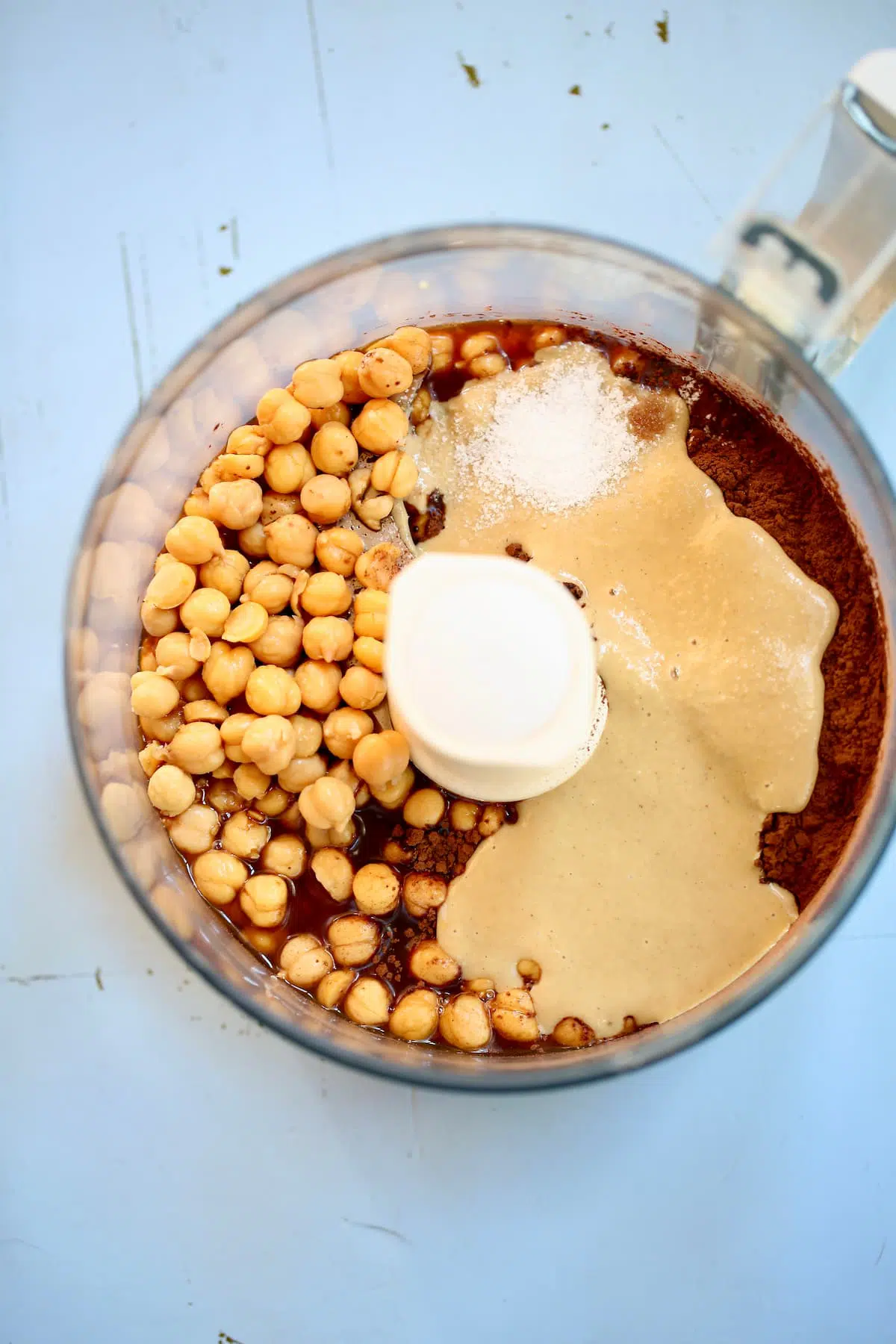 a food processor bowl of ingredients, chickpeas and cocoa powder.