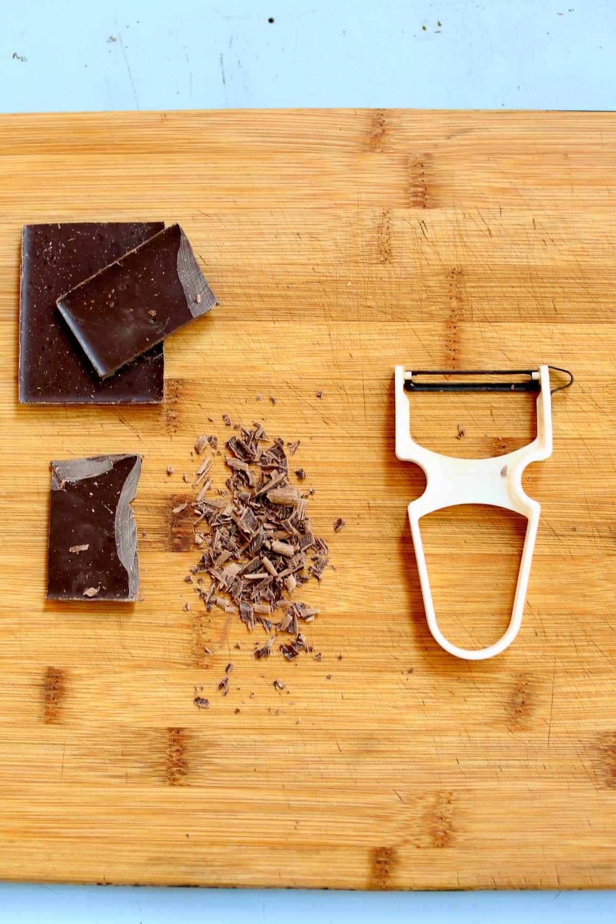 a wooden cutting board with chocolate and a vegetable peeler.