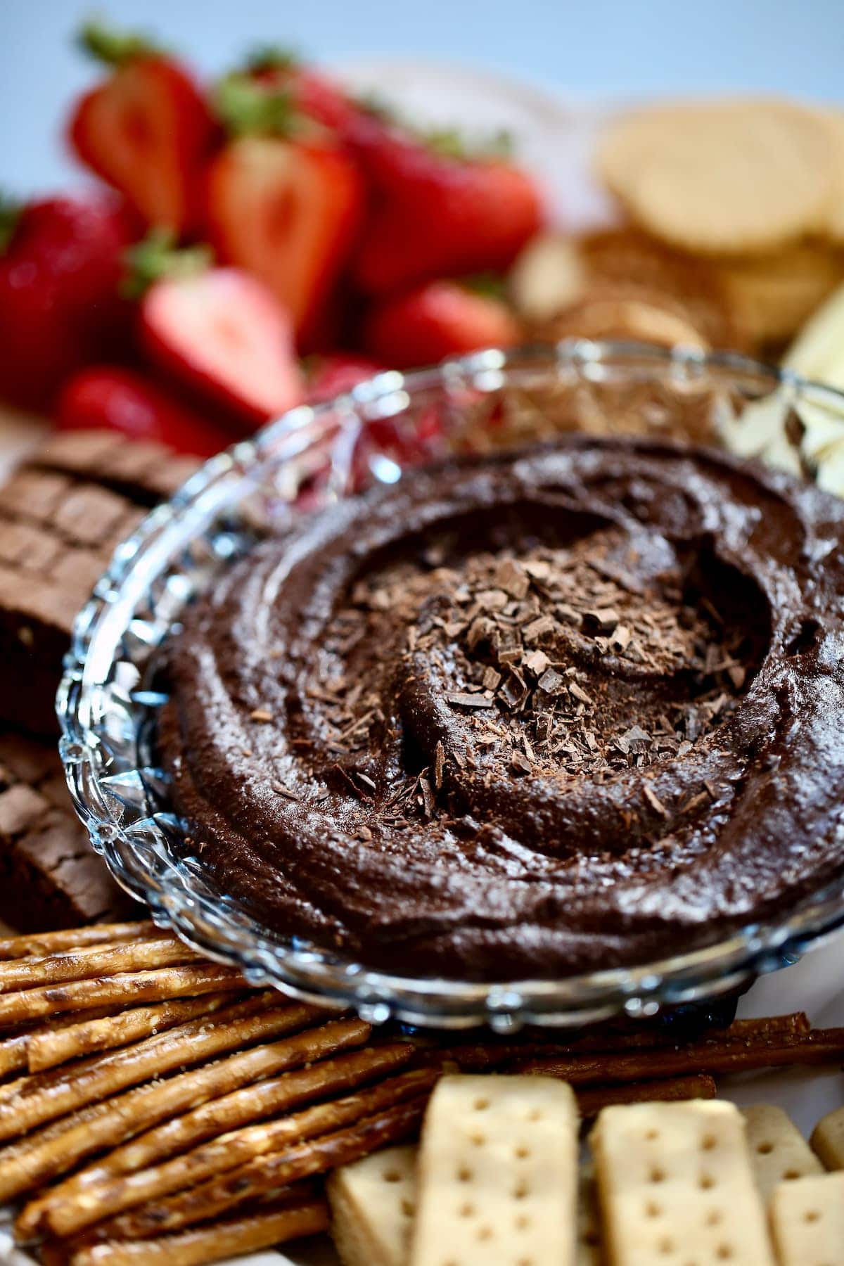 a small bowl of chocolate hummus, with fruit in the background.