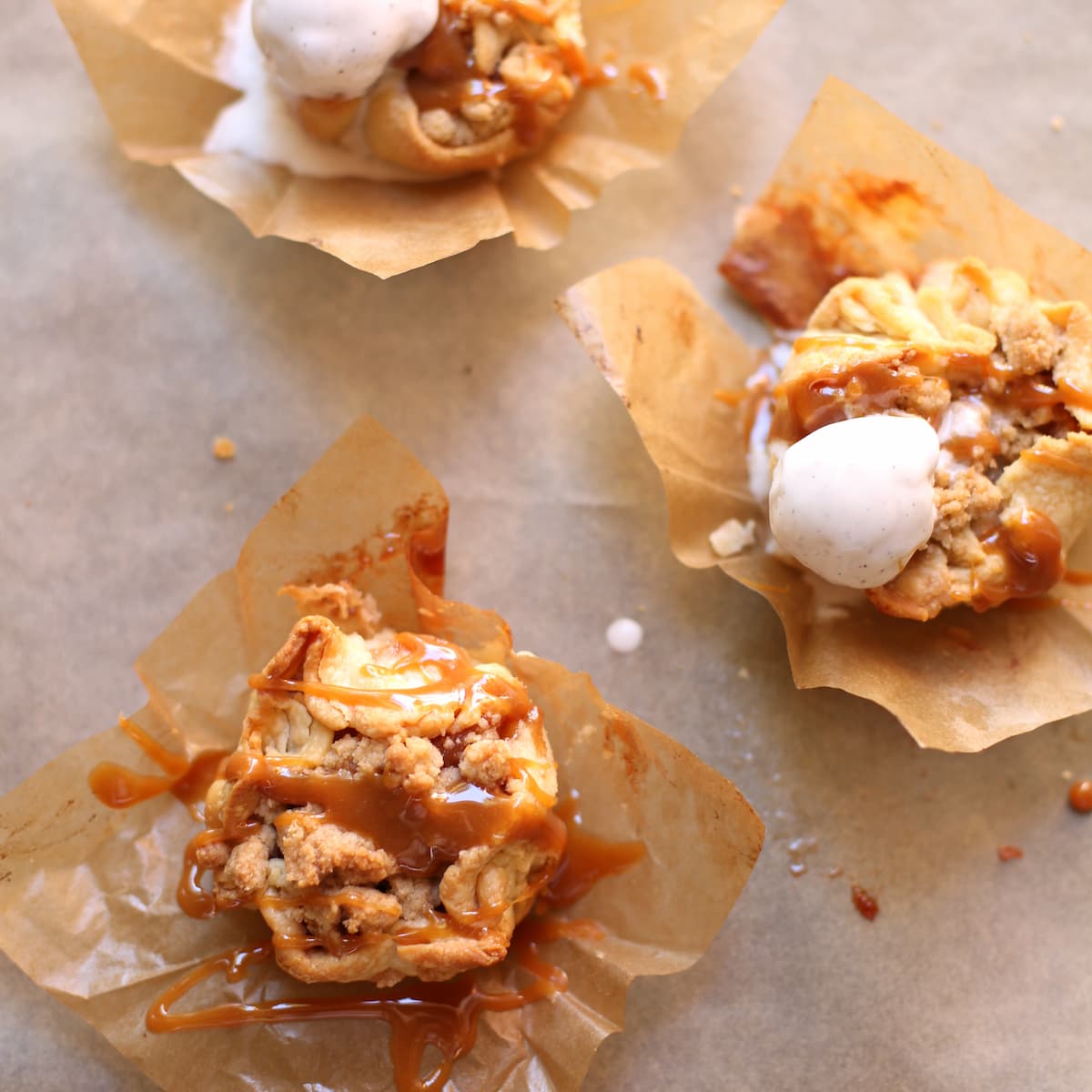 Three mini caramel apple pies on a table with ice cream on two of them.