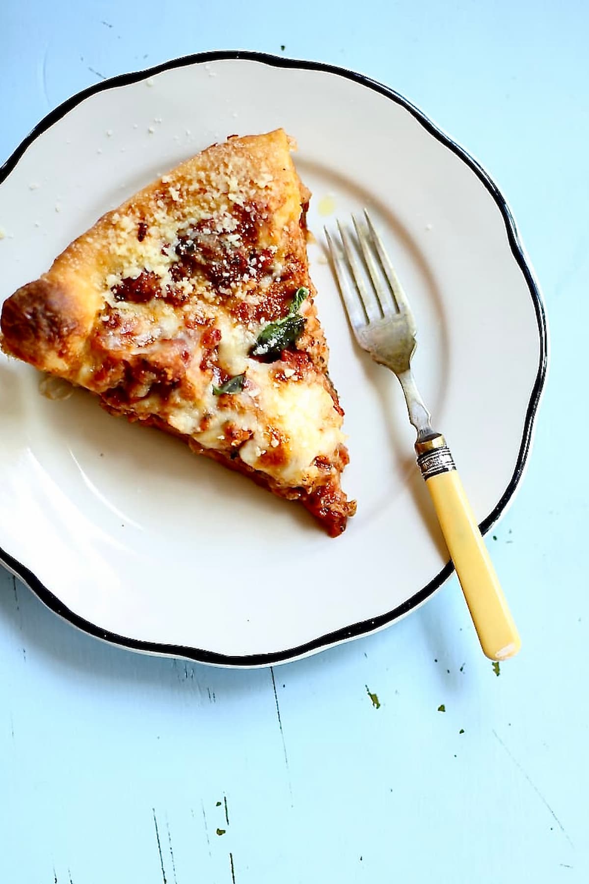 a piece of pizza on a white plate with a yellow fork on a blue table.