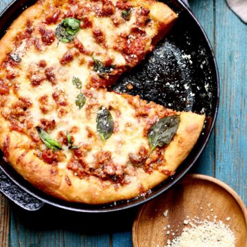 a cast iron skillet pizza with one slice out of it on a blue wooden table.