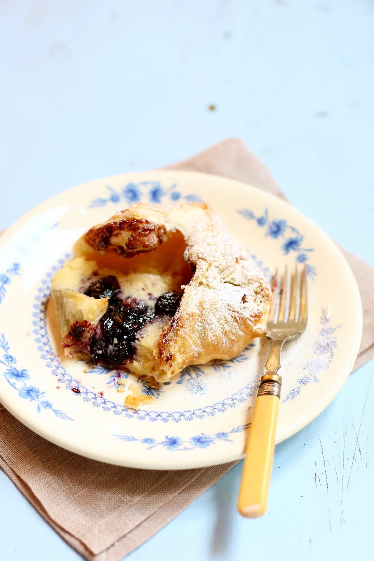 a cheese danish on a blue and white plate with a fork on a blue table.