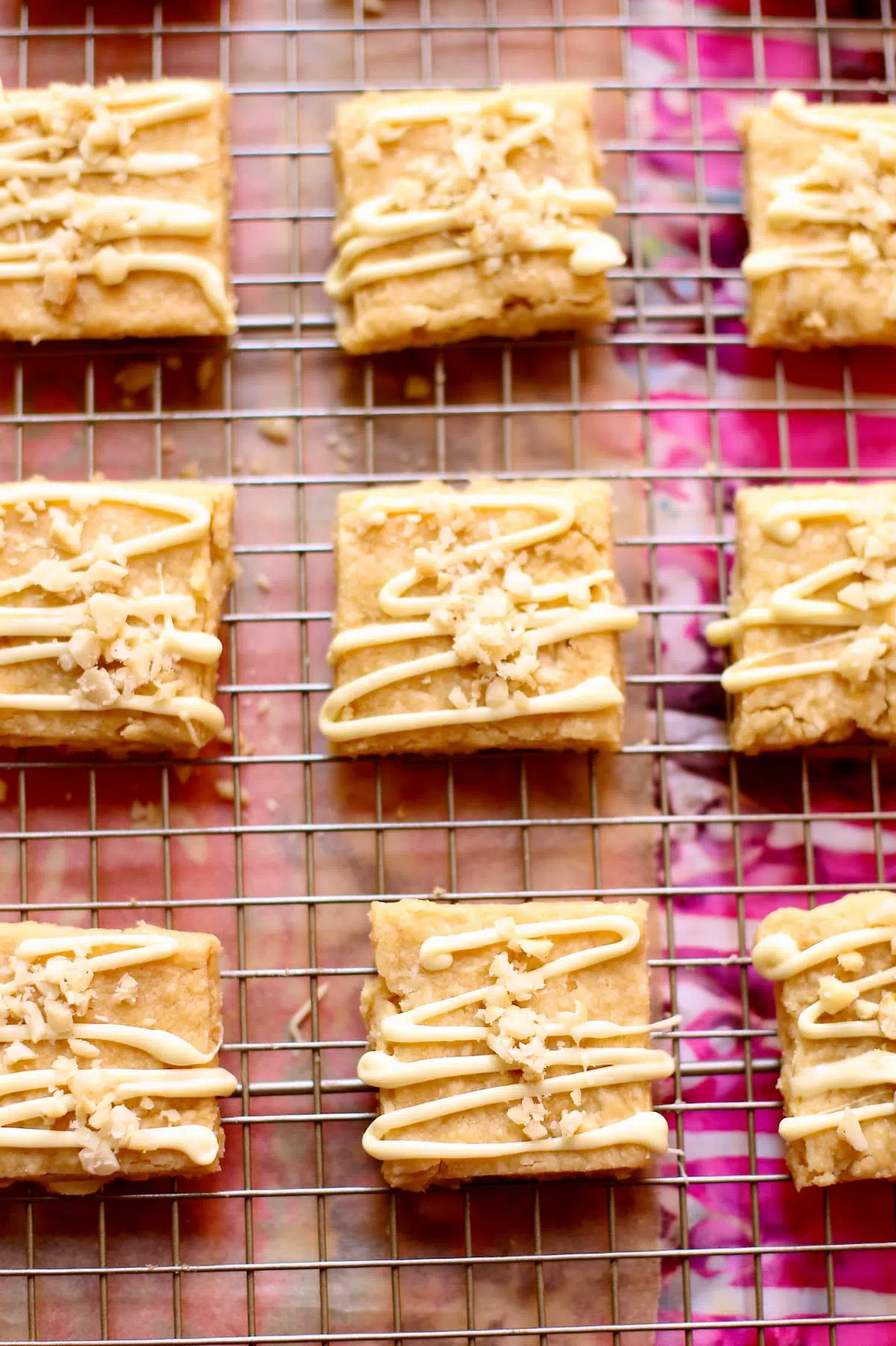 a close up of macadamia shortbread cookies on a wire rack with a pink background.