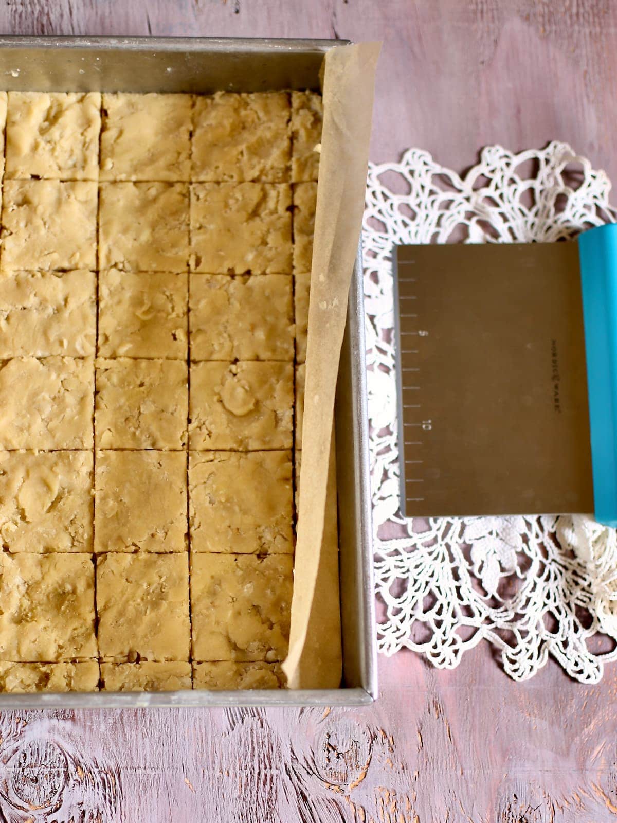 a tray of unbaked shortbread, but with a pastry scraper which is sitting right next to it.