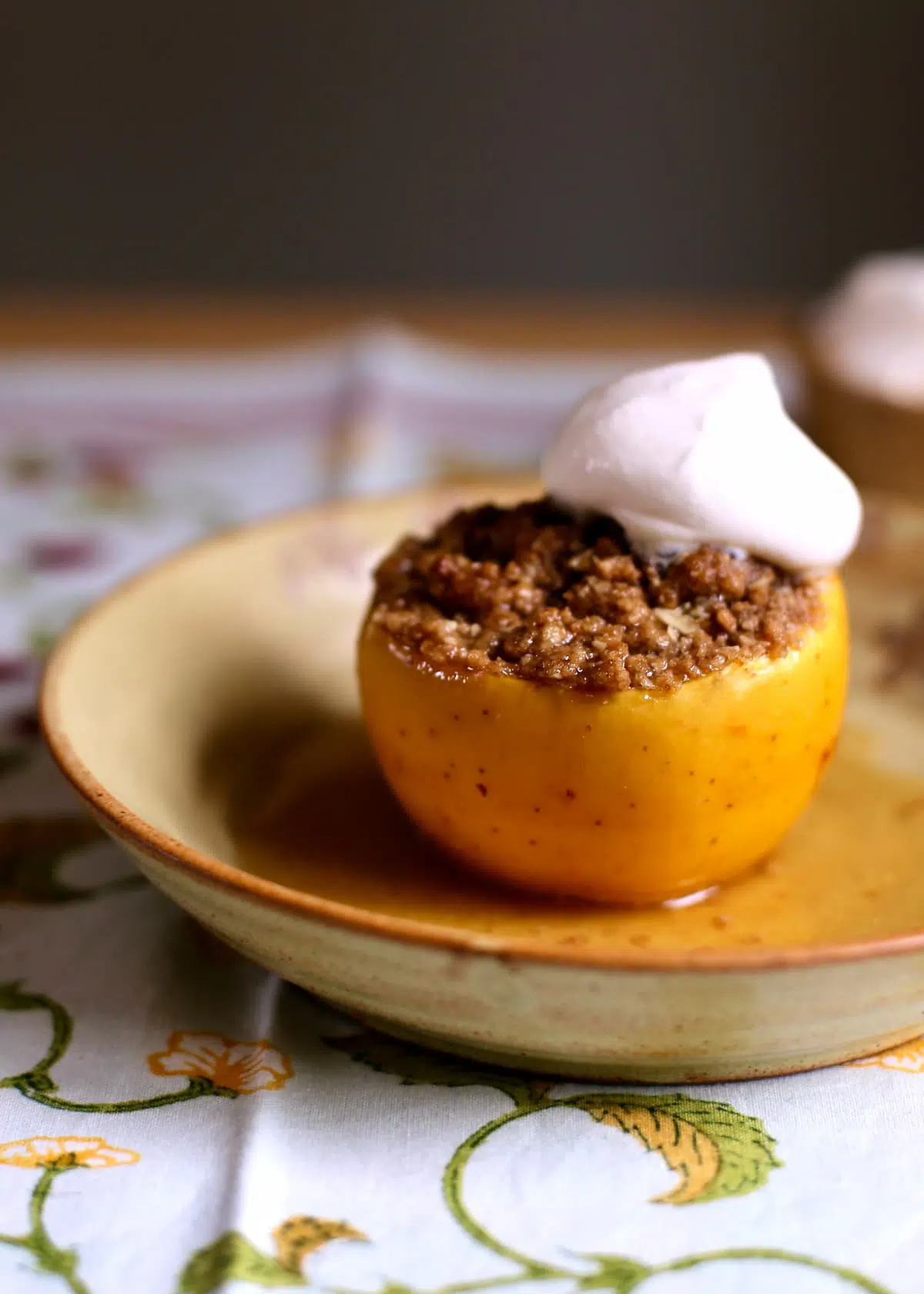 a close up shot of a baked apple with oatmeal crumble and whipped cream on a yellow plate. 
