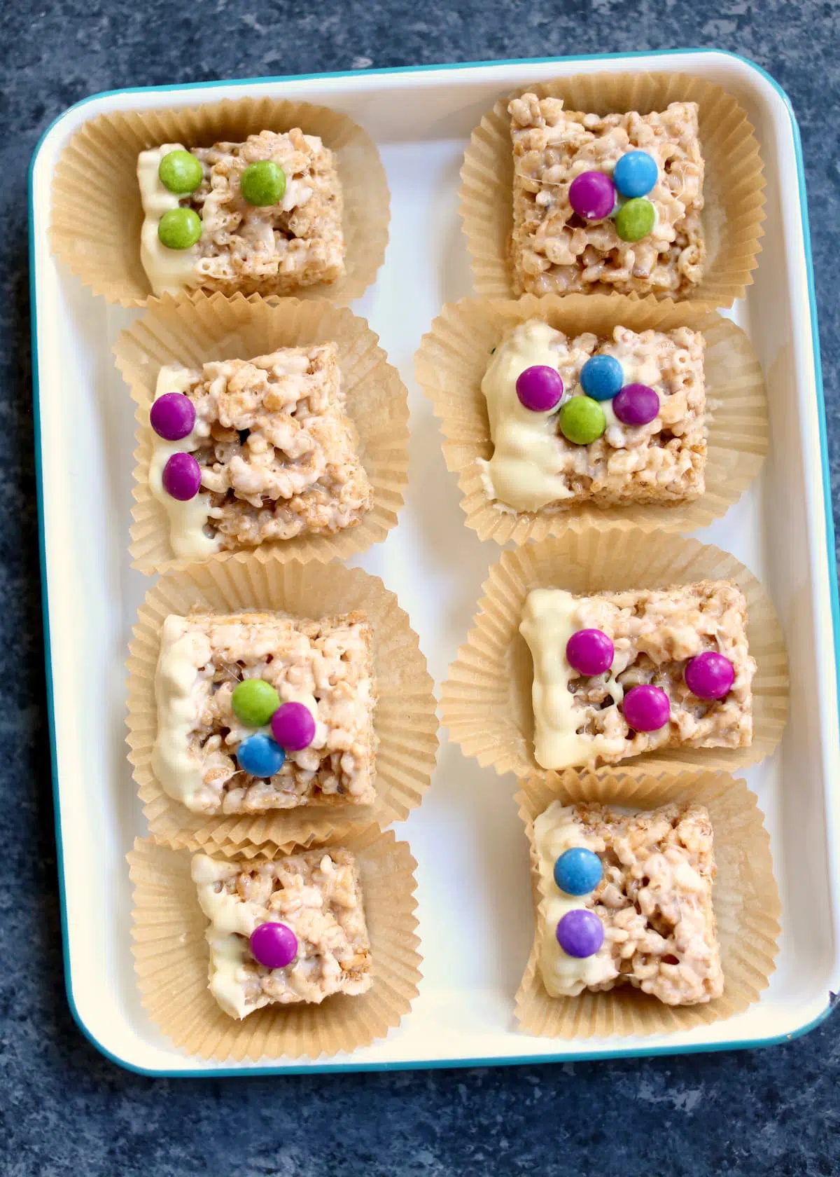 a white tray of many krispy treats with candy on top.