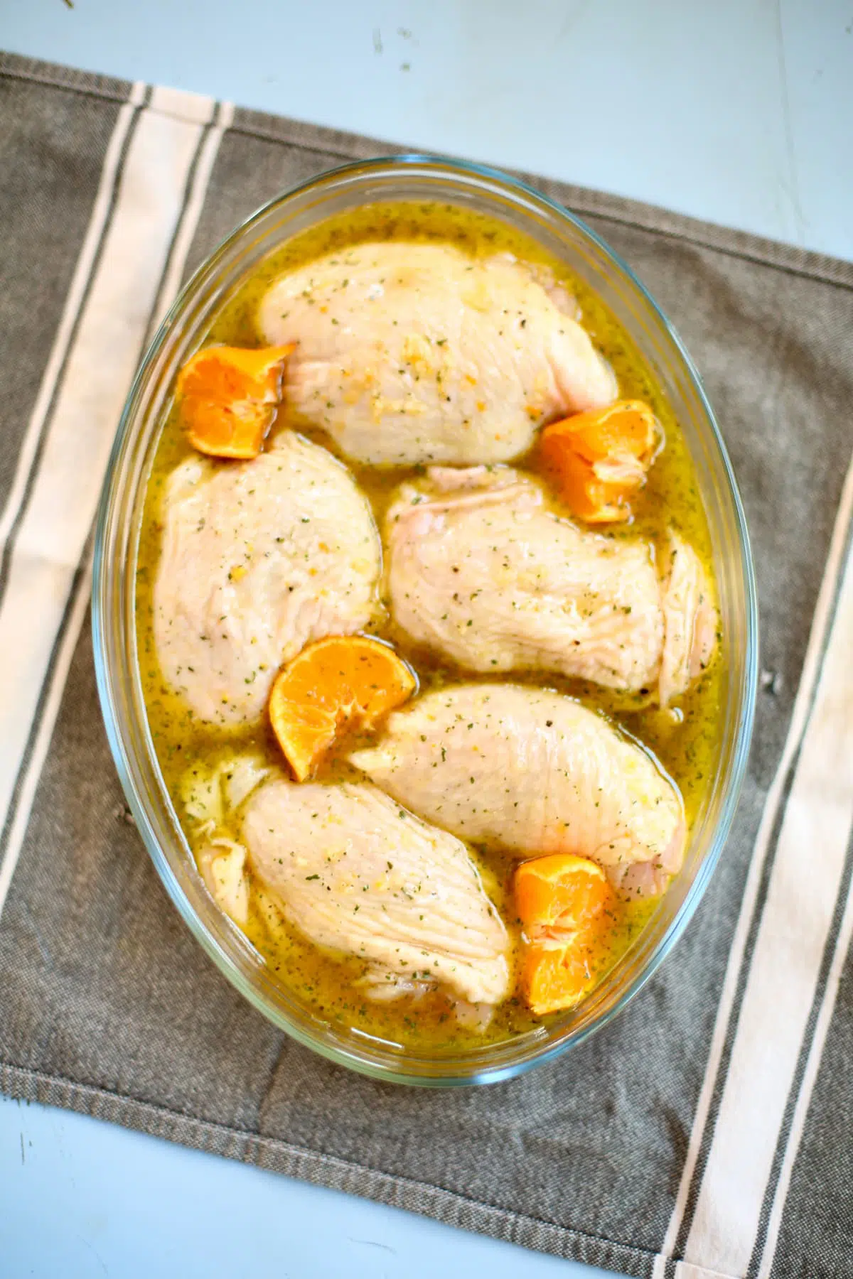 a glass dish with marinated chicken thighs in it, with citrus segments.