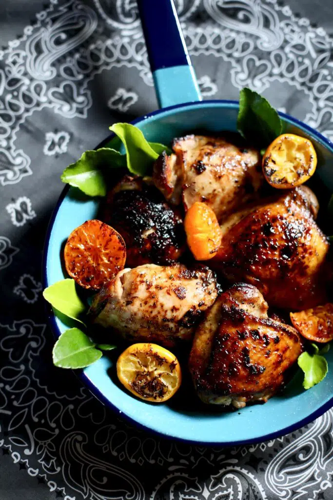 a blue skillet with citrus segments and chicken thighs on a gray tablecloth