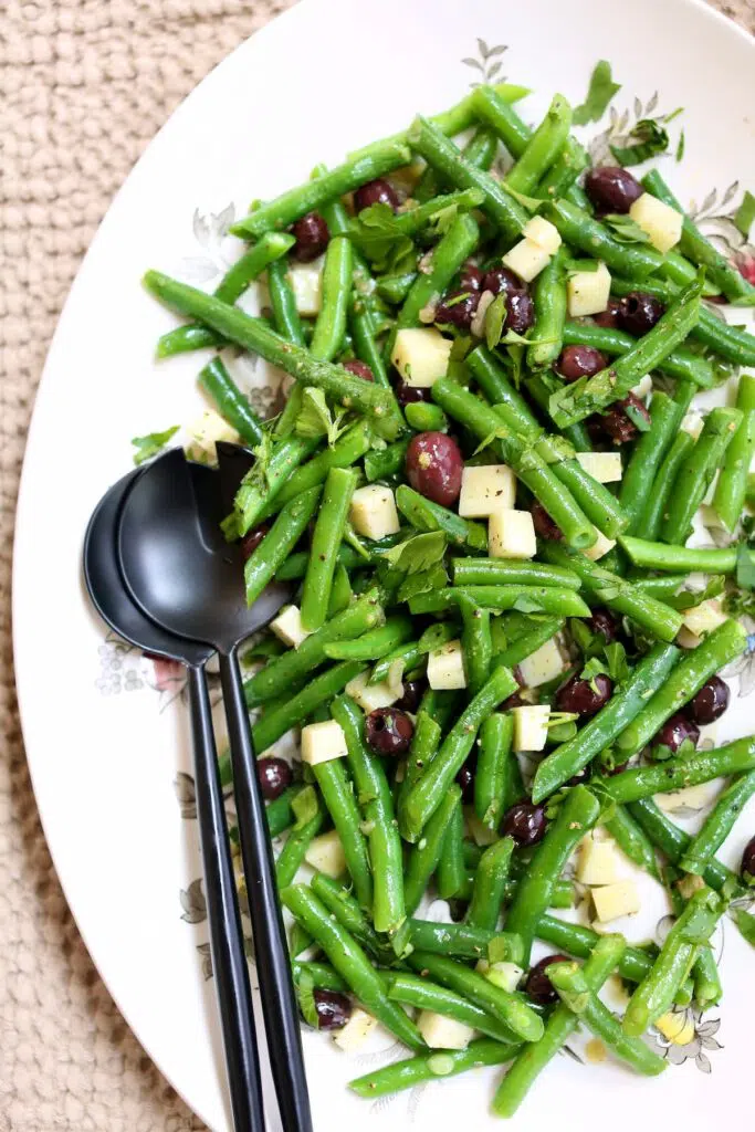 a white platter with green bean salad on it and black utinsils