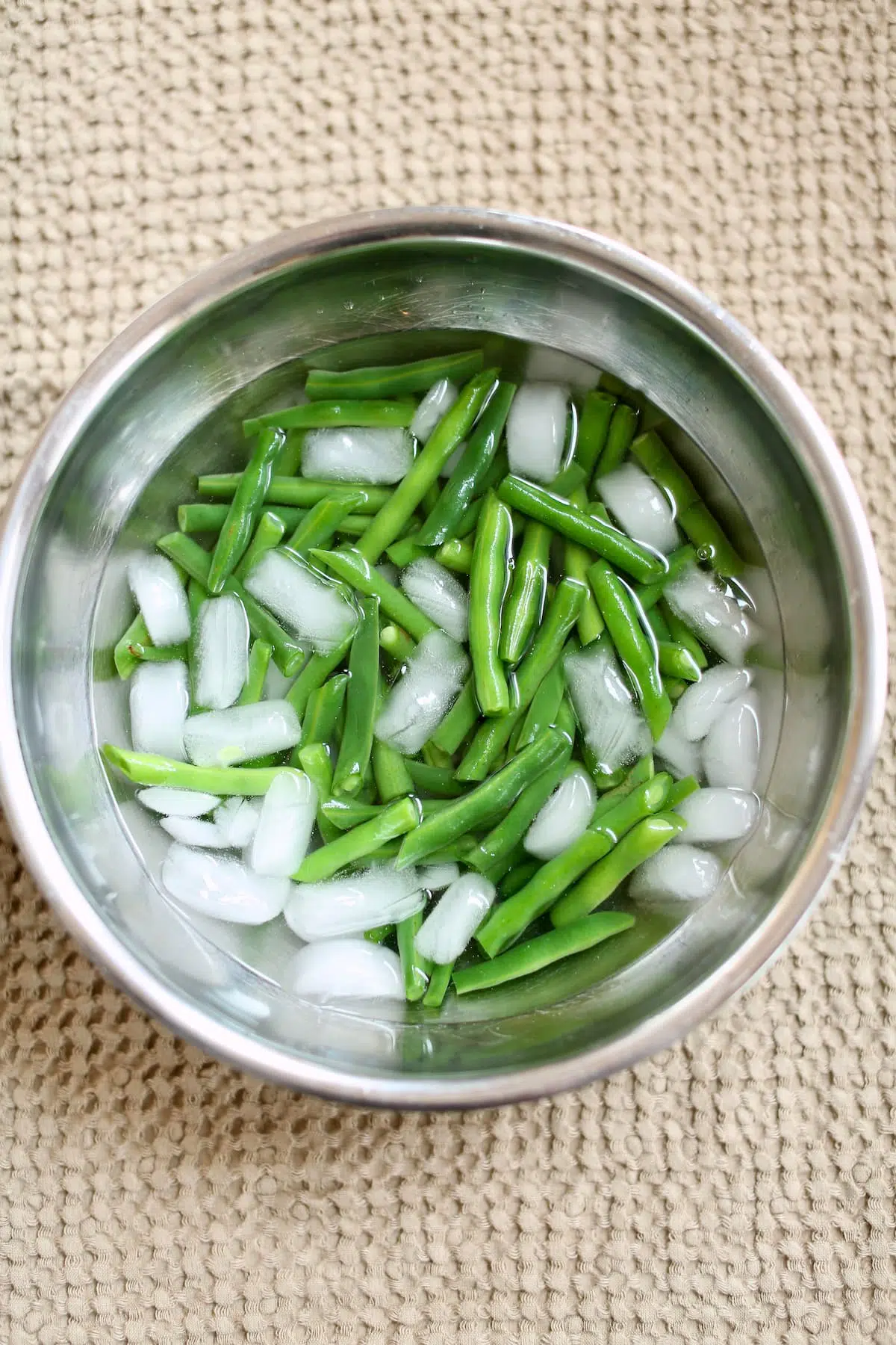 a large silver bowl with green beans and ice water in it.