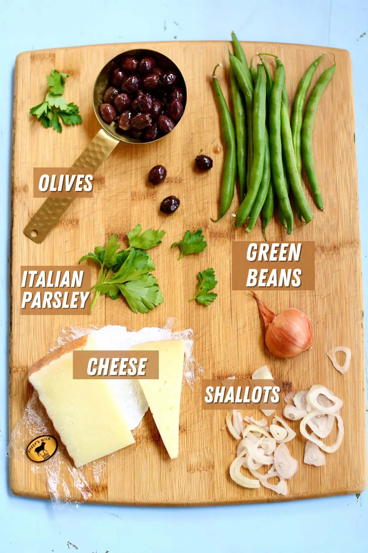 a wooden cutting board with ingredients on it for green bean salad, with text overlay sayiing the ingredient names.