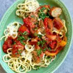 a green plate of sausage and vegetables with noodles.