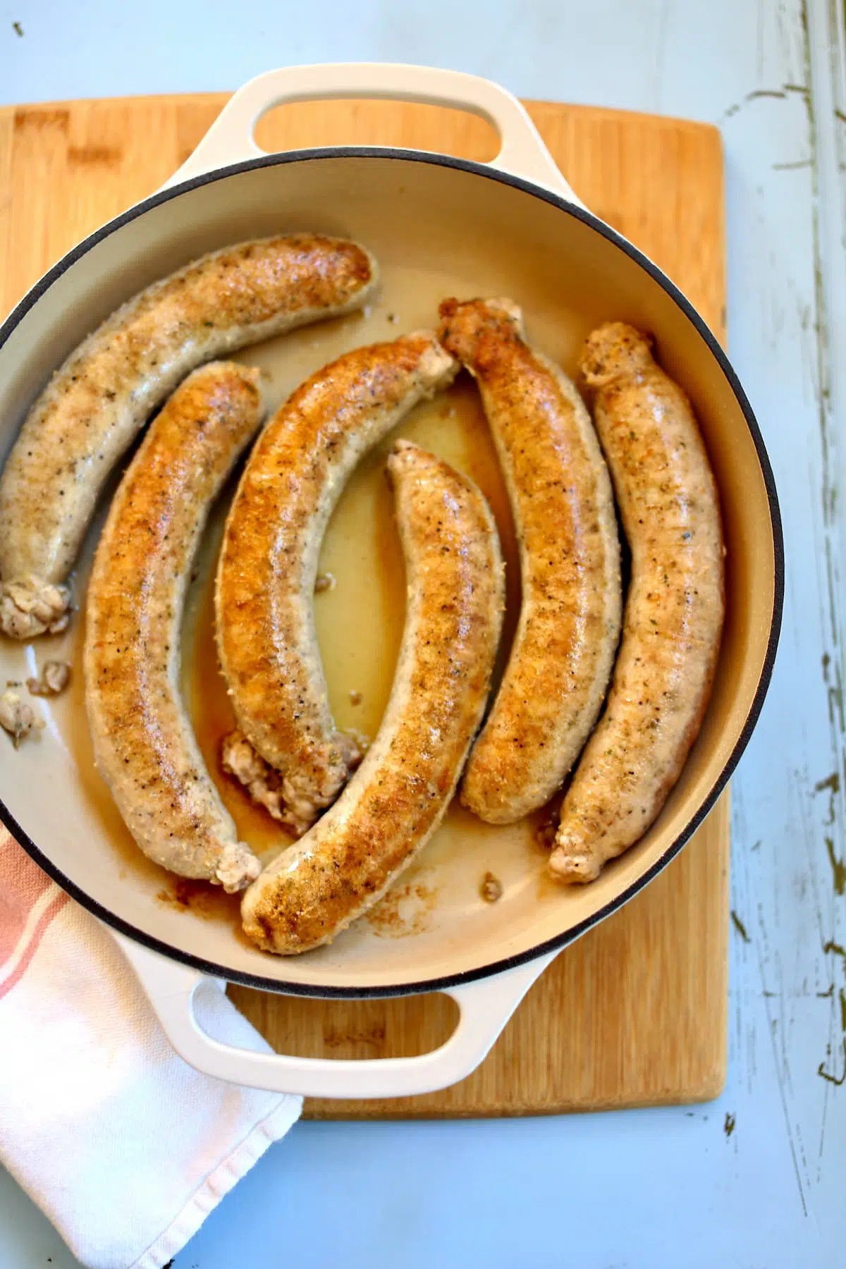 sausages getting browned in a skillet, on a blue table