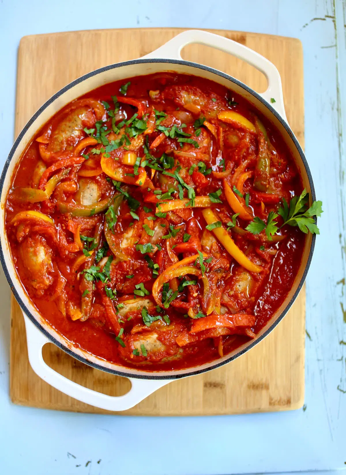 a skillet with sausage and vegetables on a cutting board.