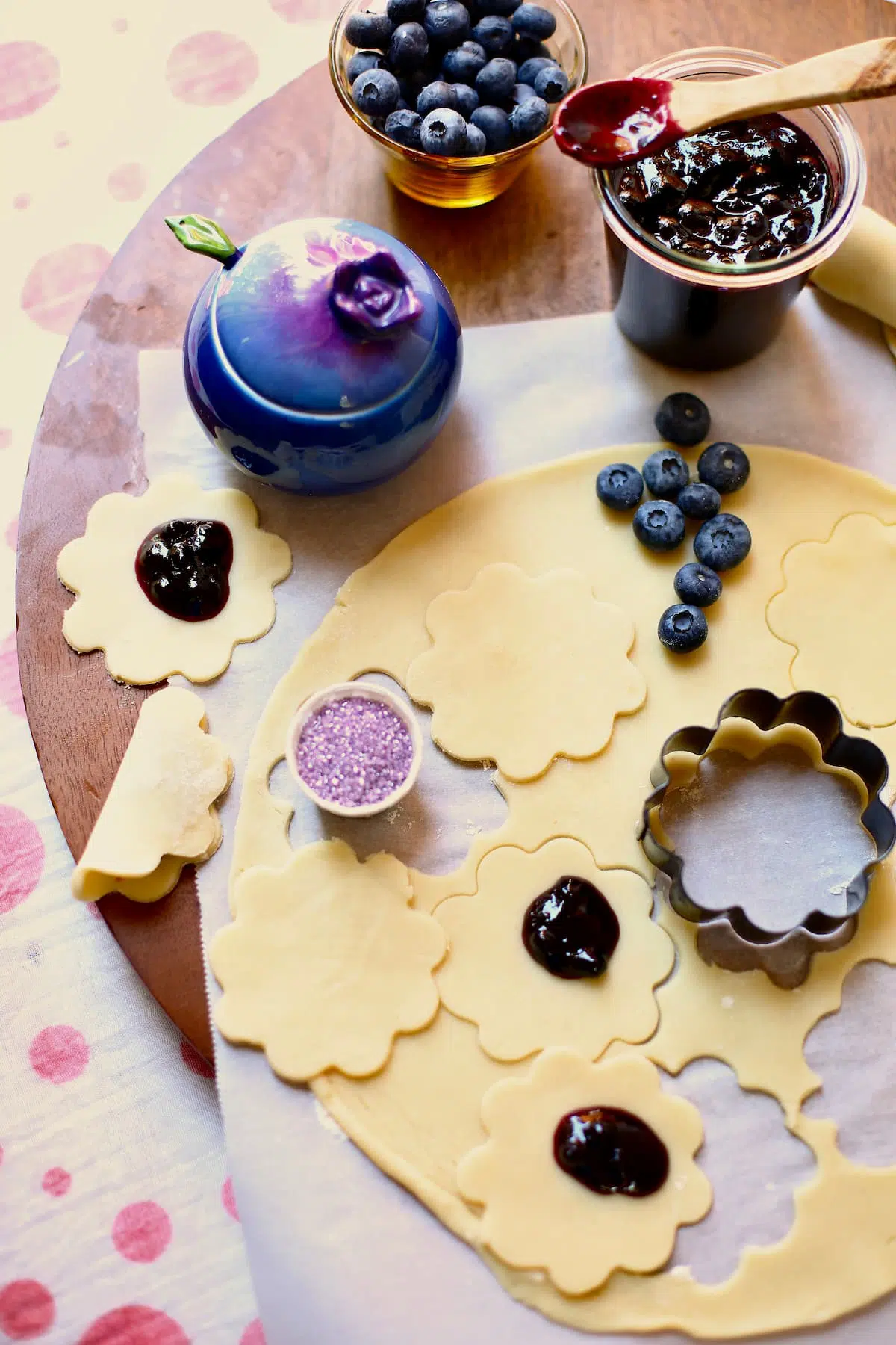 a cutting board with pie crust, blueberries, jam and spinkles and a cookie cutter.