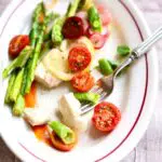 a white platter with chicken and vegetables and a fork on it and text overlay.