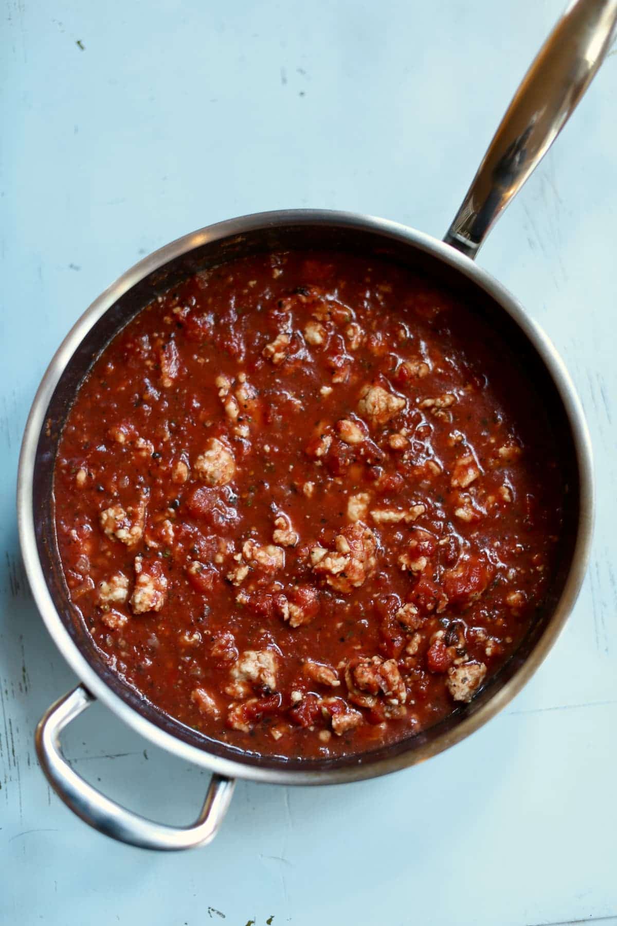 a skillet with red sauce and ground turkey.