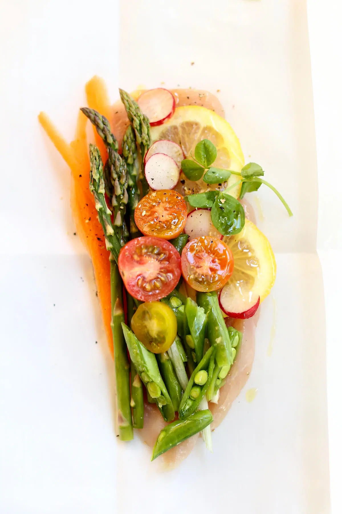 a raw chicken breast with vegetables on it, on parchment paper.