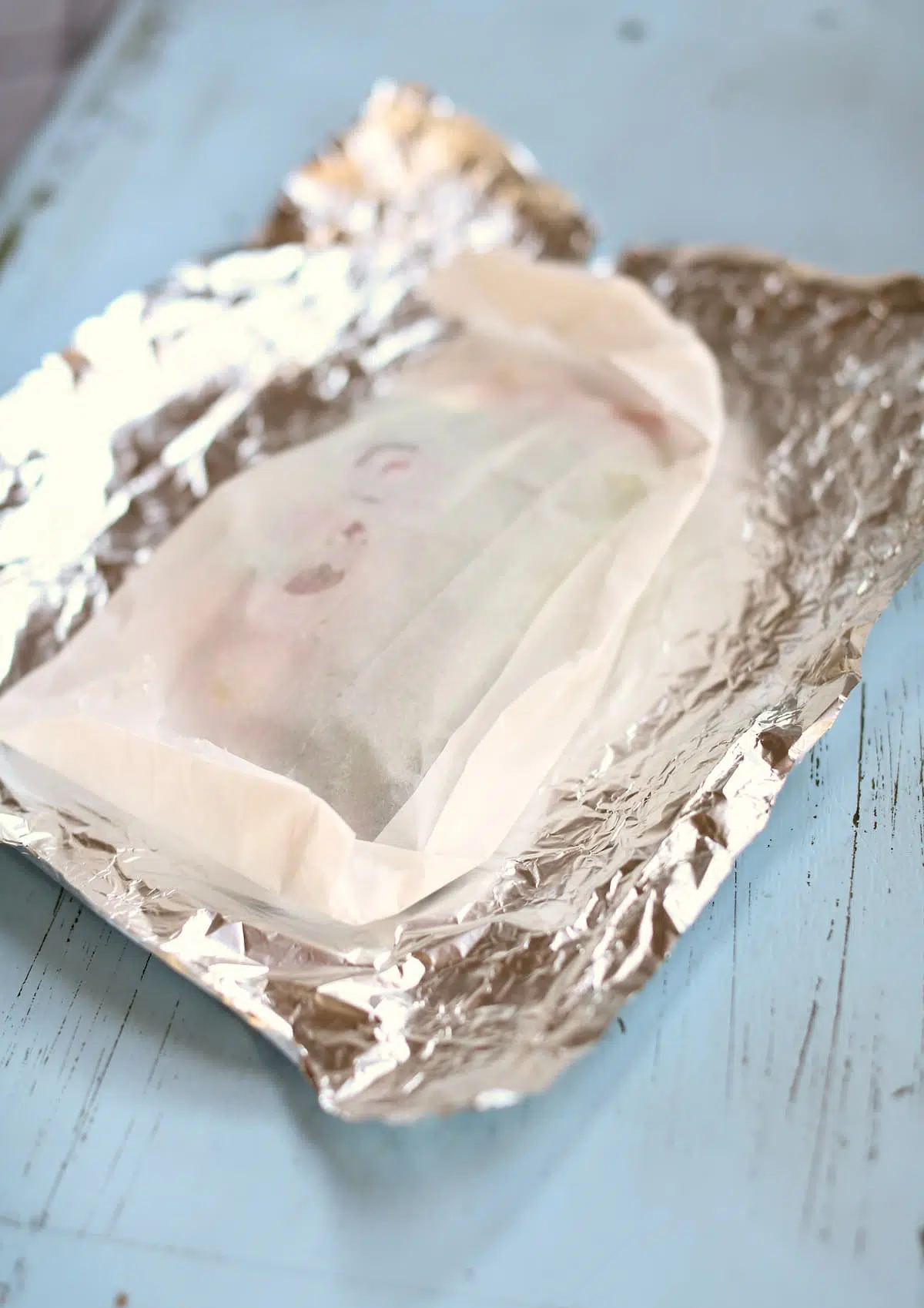a picture of parchment and tin foil wrapped chicken before it's fulling wrapped.