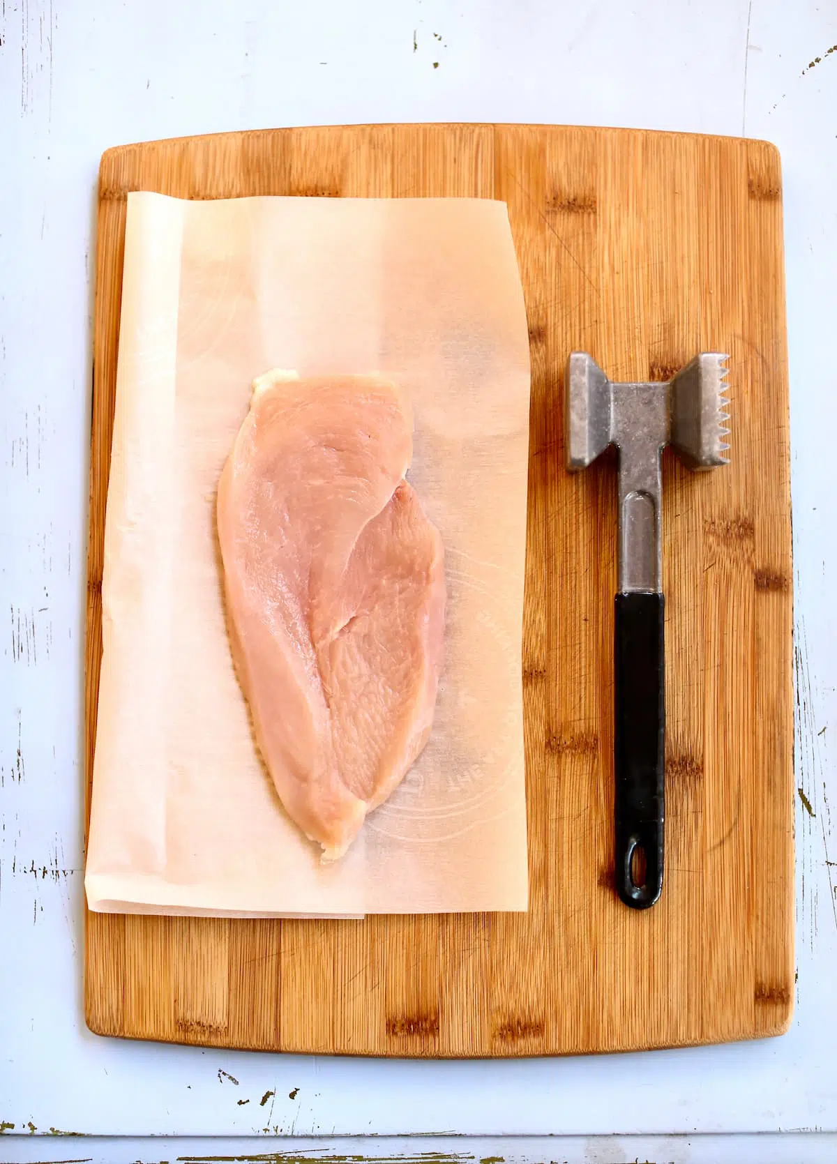 a cutting board with a piece of chicken on it and a mallet.
