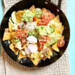 a skillet of nachos on a table with a cloth underneath it.