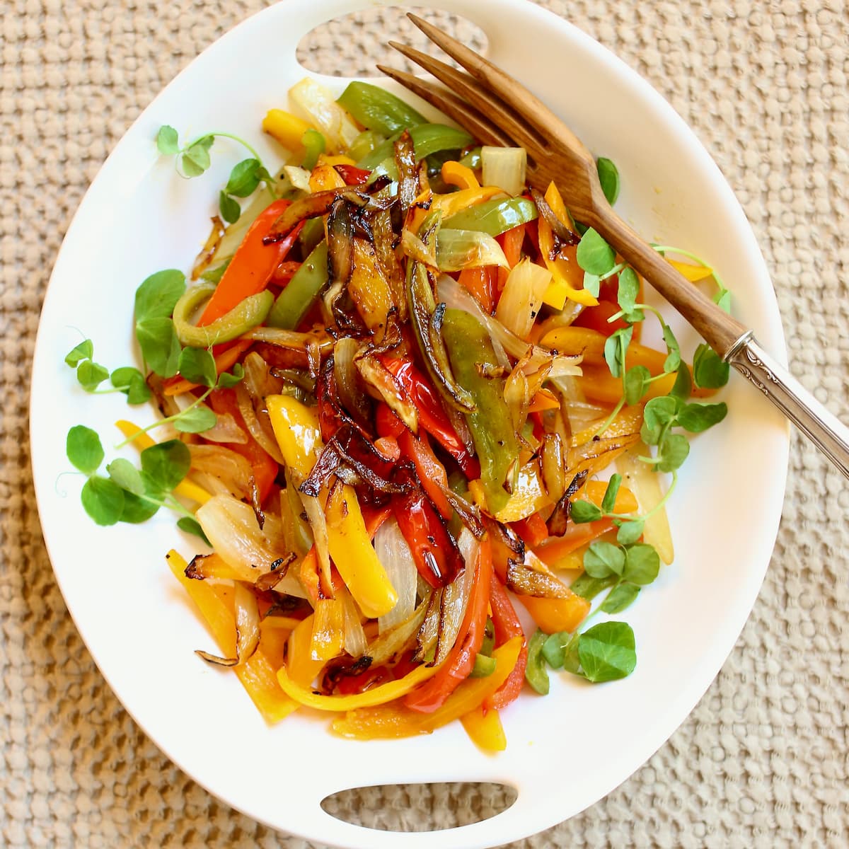 a white platter of grilled peppers and onions with a serving fork alongside.