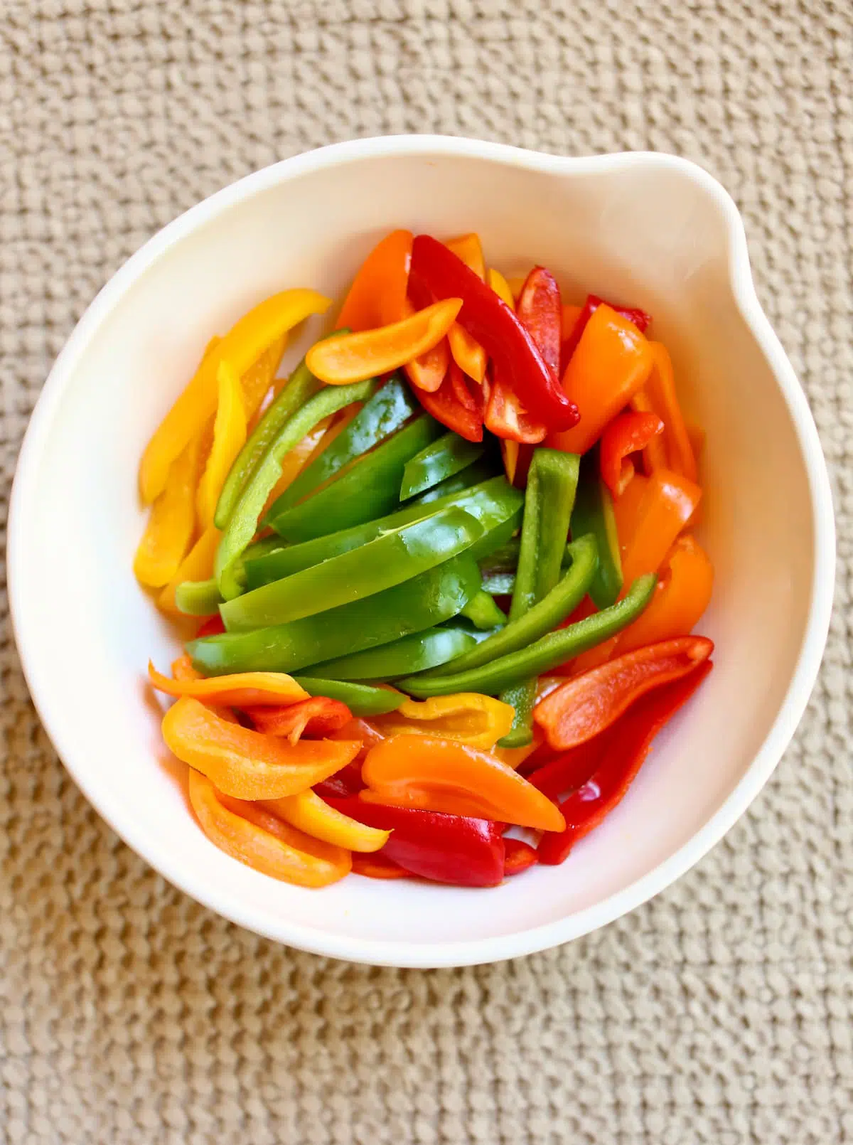 a white bowl of sliced colored peppers.