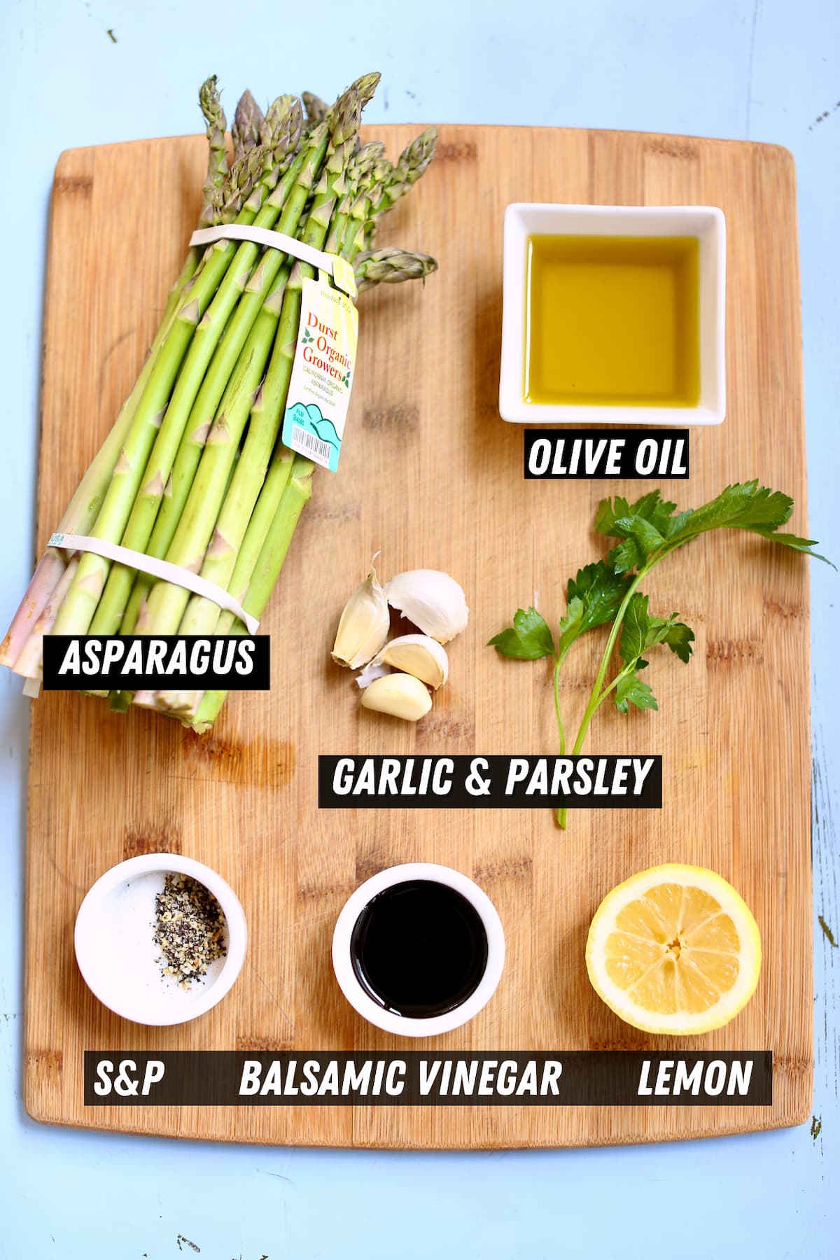 a cutting board with ingredeints like asparagus, parsley, olive oil and seasonings