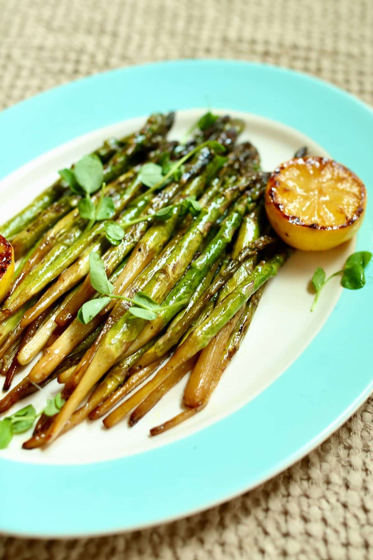 a side angle shot of asparagus on a platter with grilled lemon.