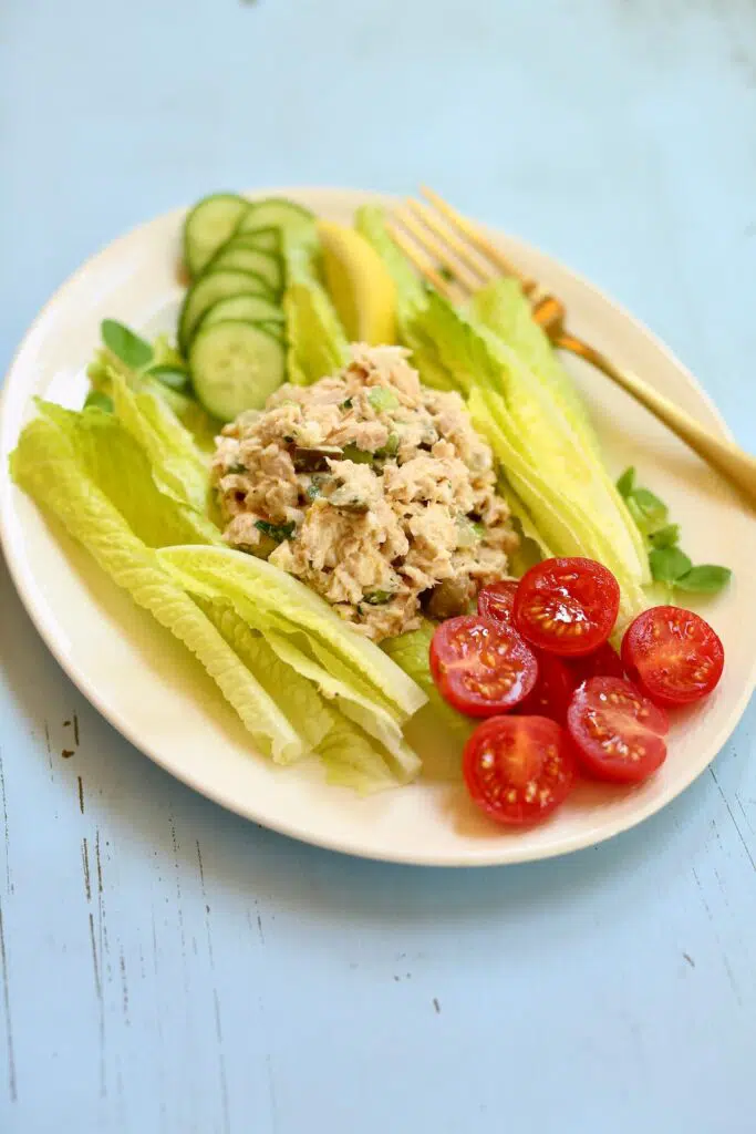 a palte of tuna salad and vegetables on a white platter, side view.