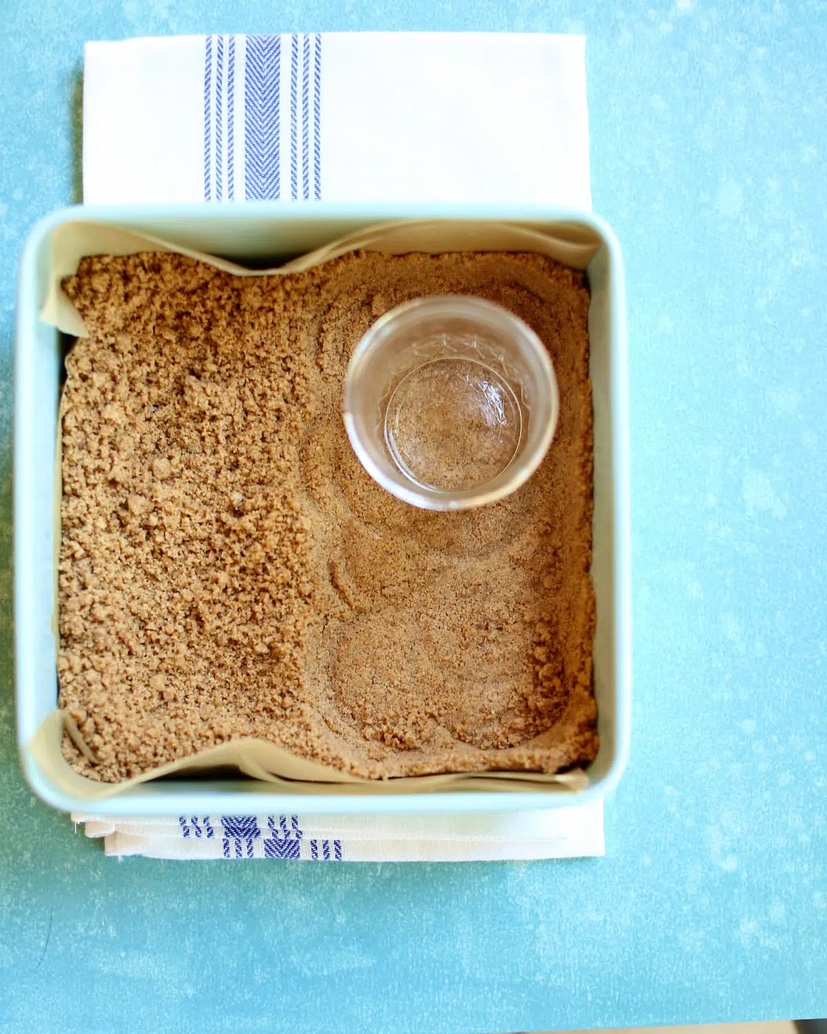 a square baking pan with graham cracker crumbs in it and a jar.