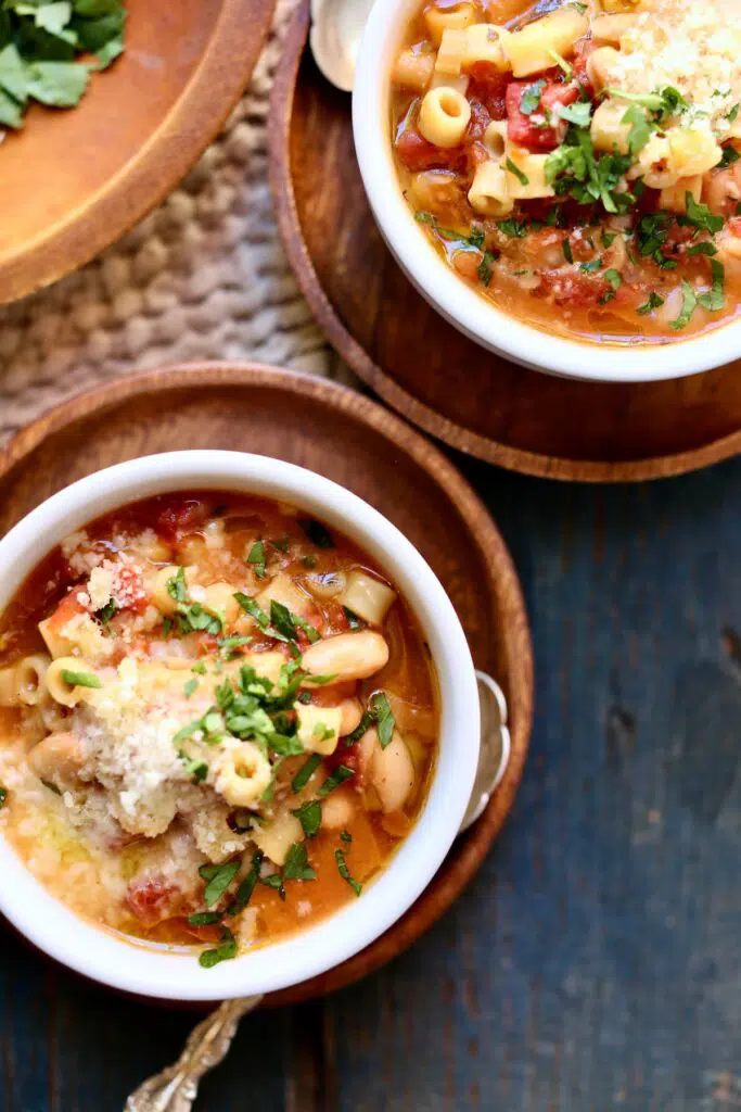 two bowls of soup, one wooden plate of cheese and parsley on a table.