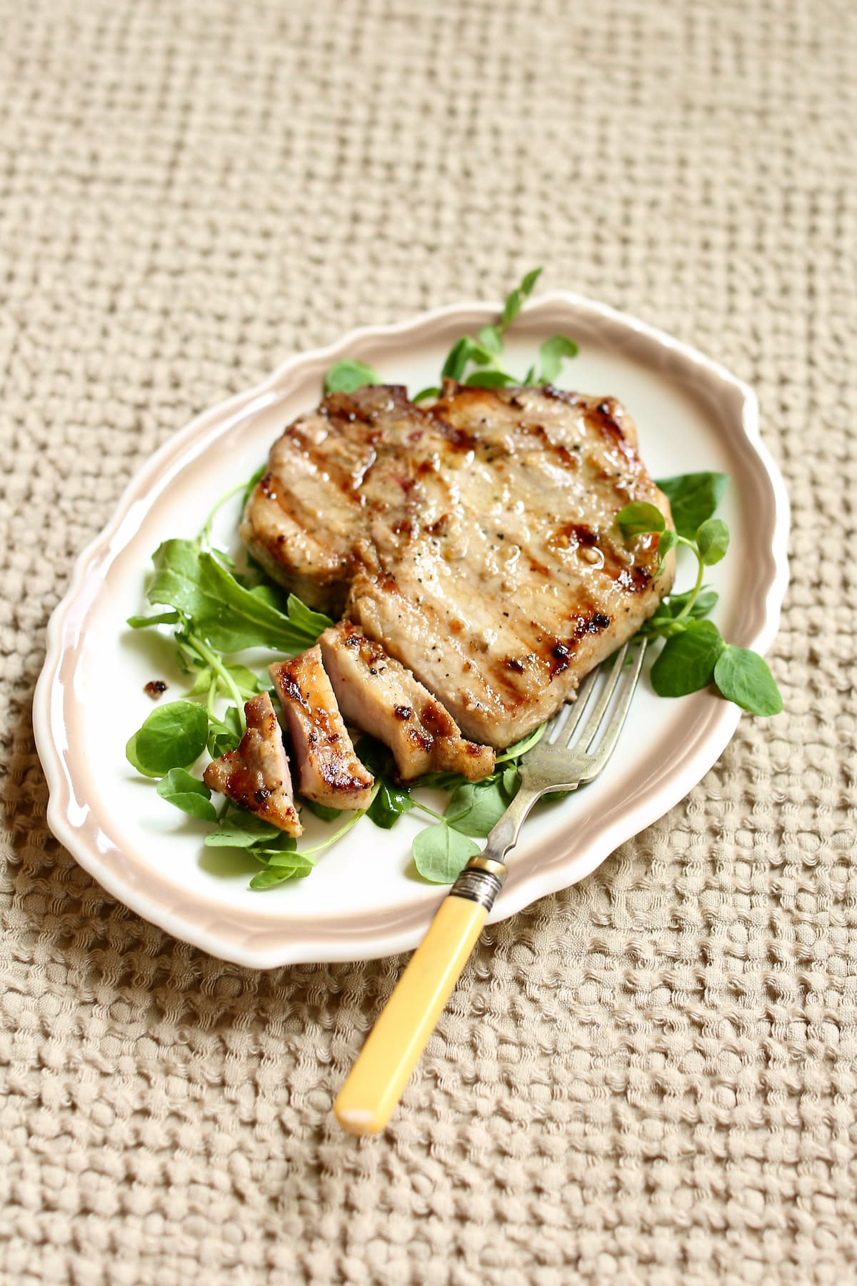 a pork chop, partially sliced on a table with a fork.