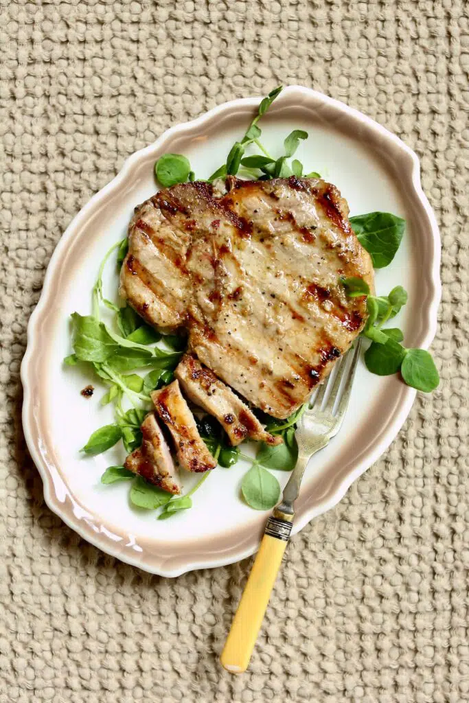 a white plate with tan trim with a pork chop on it and a fork