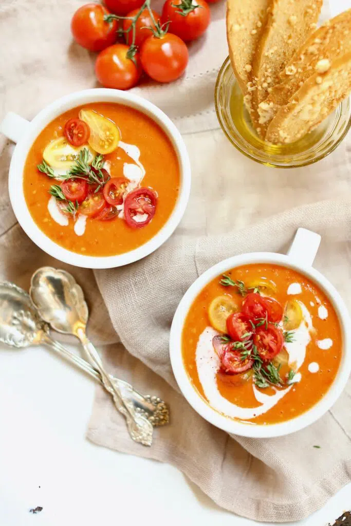 two white bowls with handles of tomato soup and two spoons.