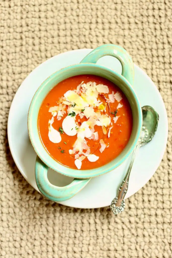 a blue tureen of tomato soup sitting on a white plate with a spoon next to it.