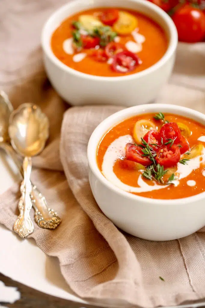 a side view photo of two bowls of tomato soup and two spoons on a napkin.