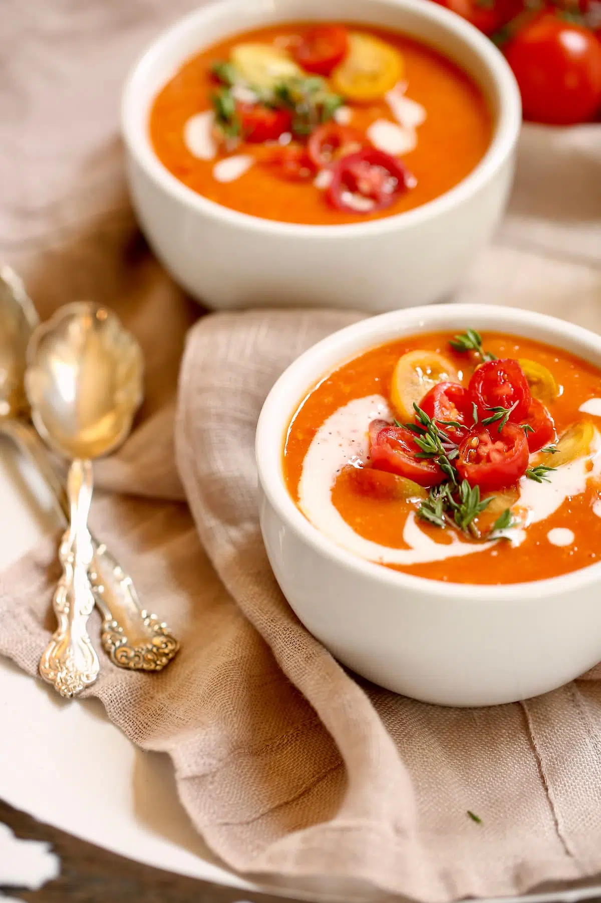 a side view photo of two bowls of tomato soup and two spoons on a napkin.