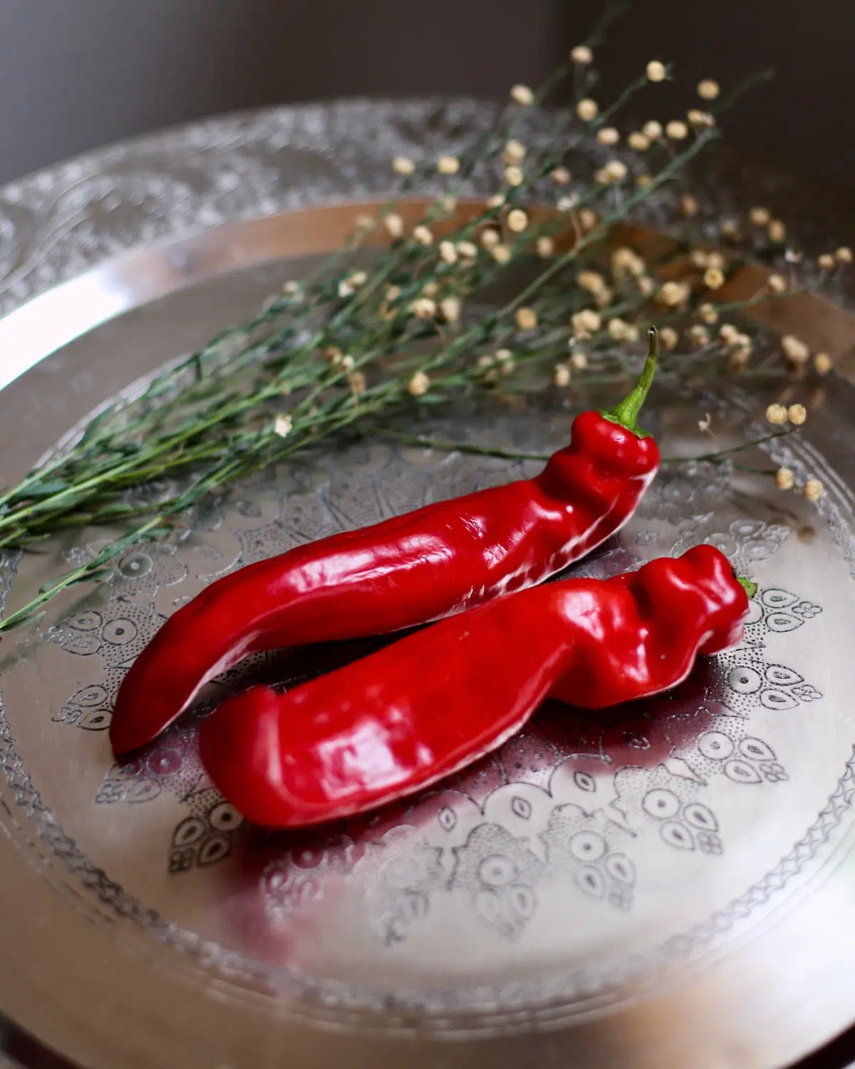 a couple of red anaheim chilis on a silver platter.