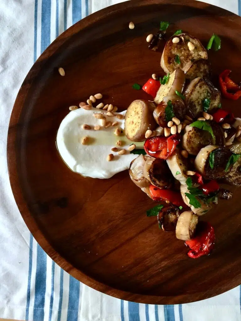 a wooden plate with cooked eggplant and greek yogurt.