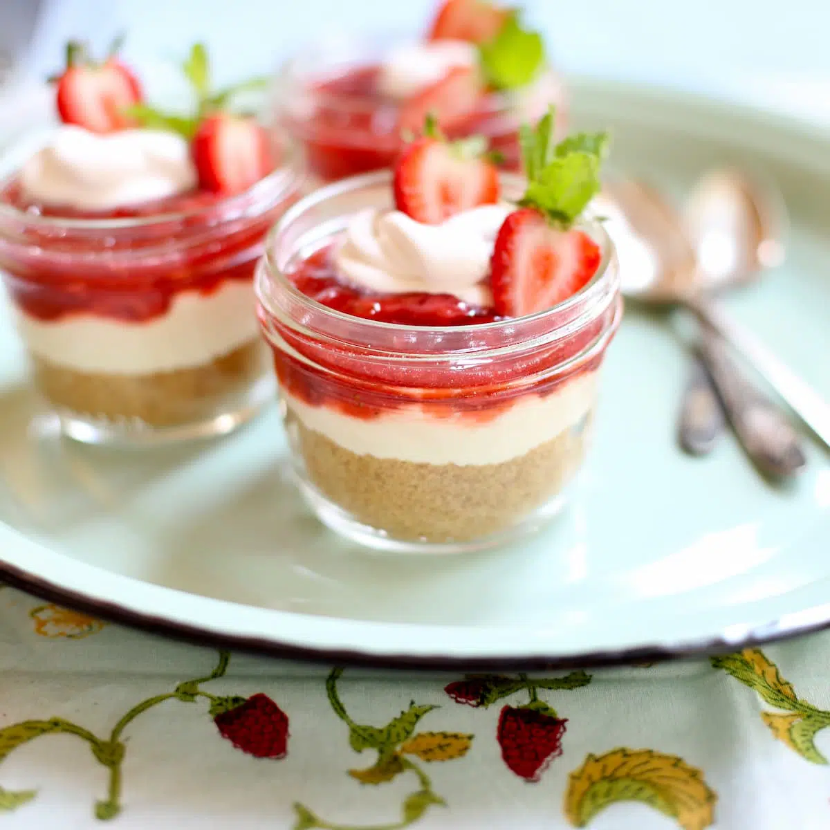 a blue tray with strawberry cheesecake desserts on it with some spoons.