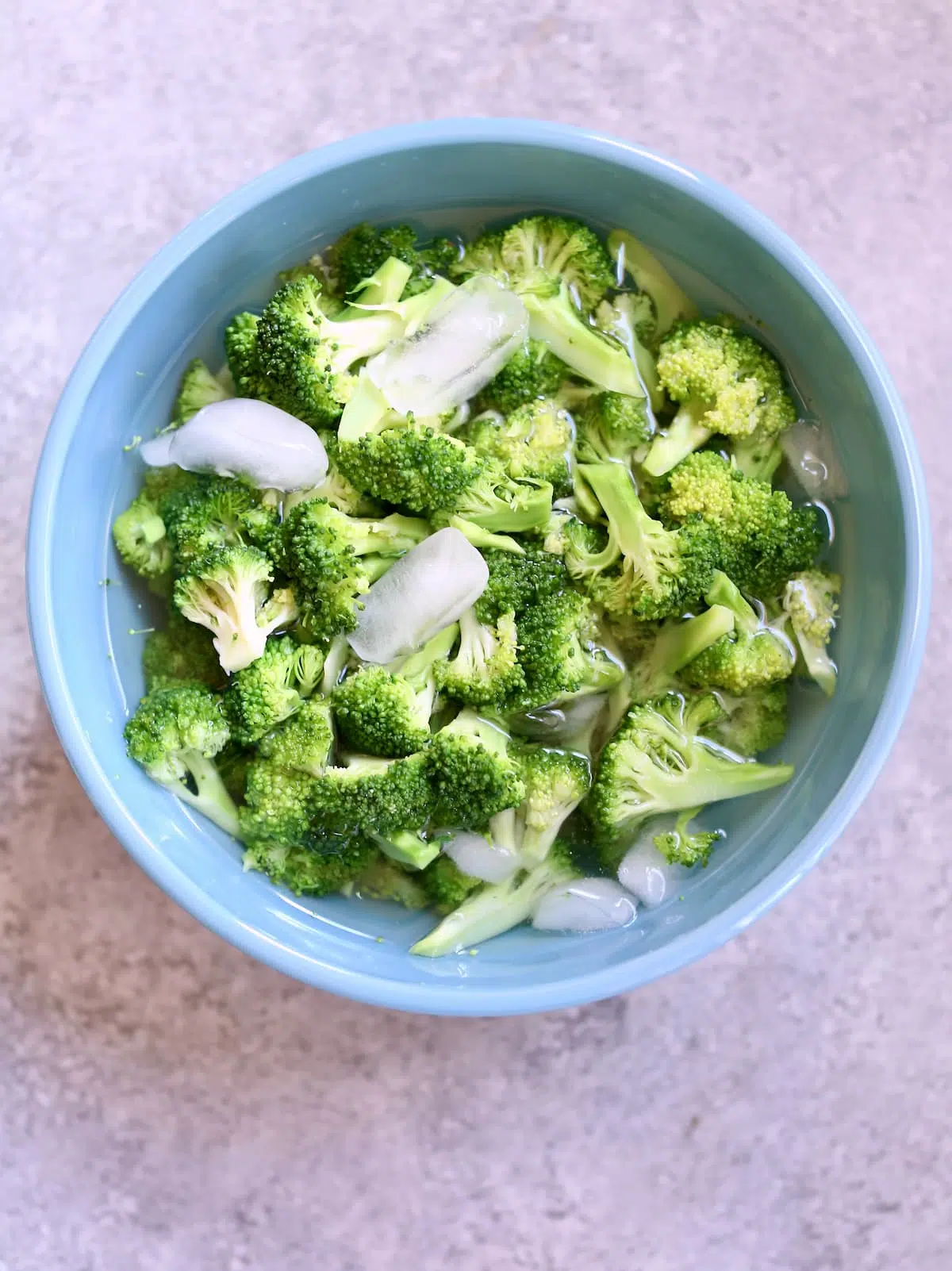 a blue bowl with broccoli in ice water.