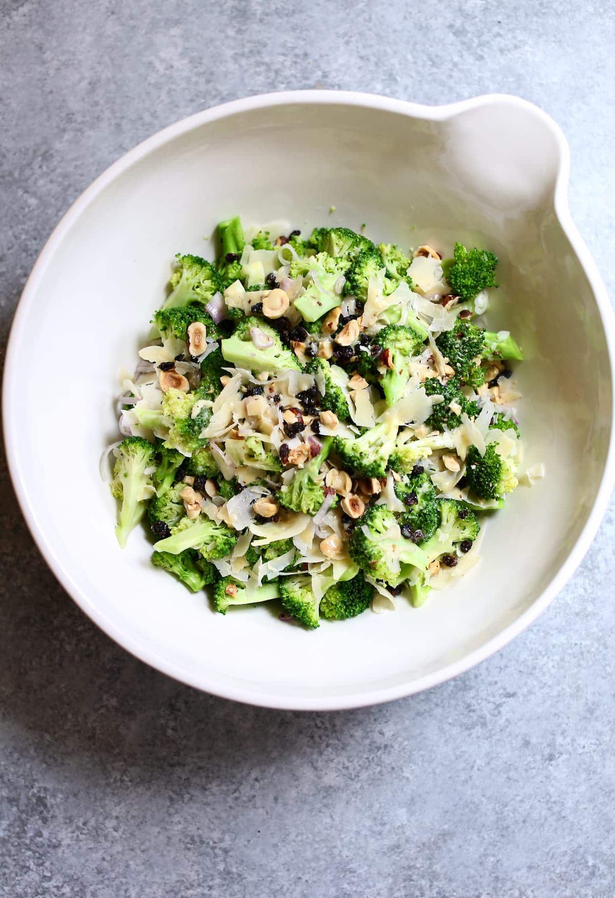 a white bowl of broccoli salad on a gray table.