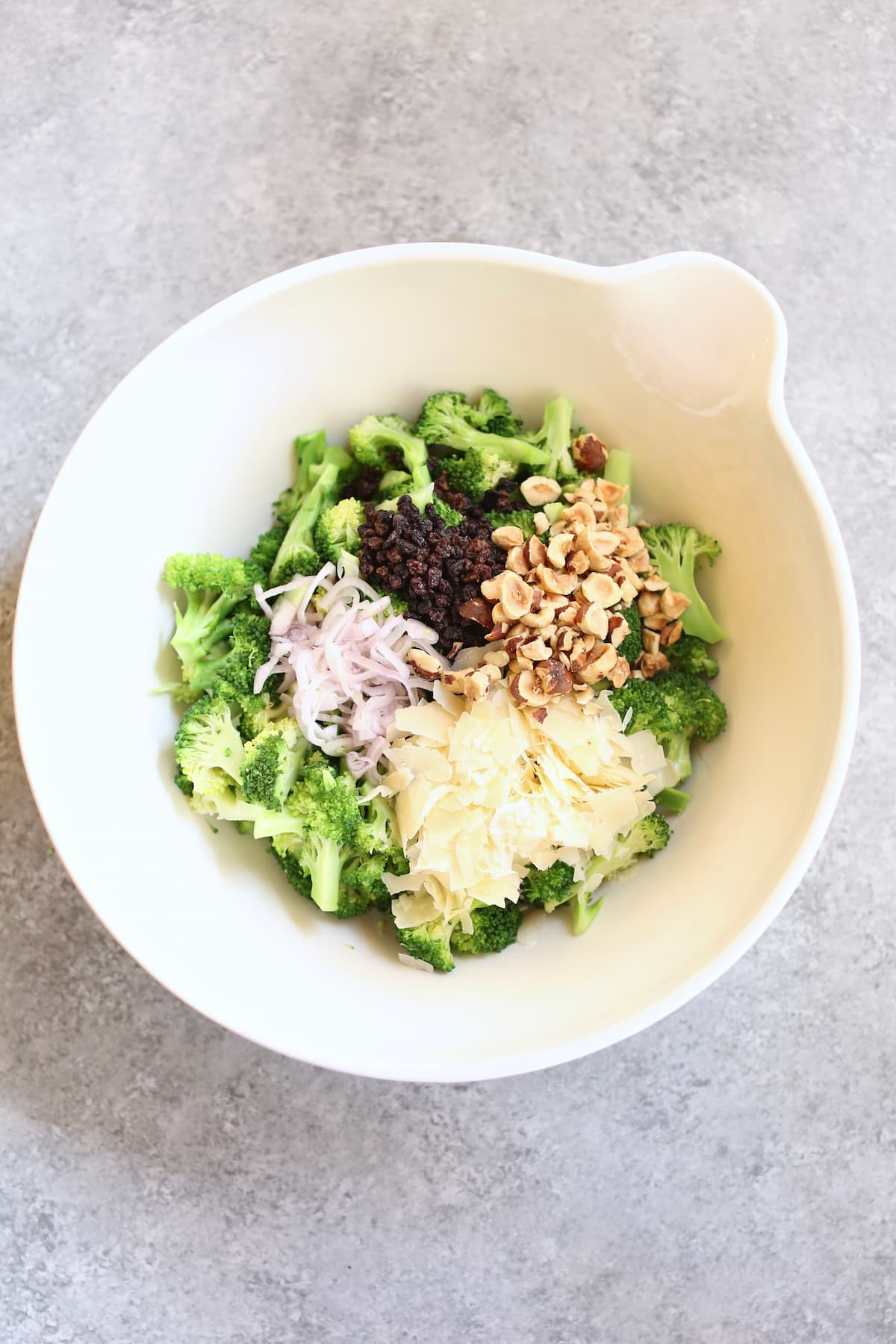 a white bowl with unmixed ingredients for broccoli salad in it.